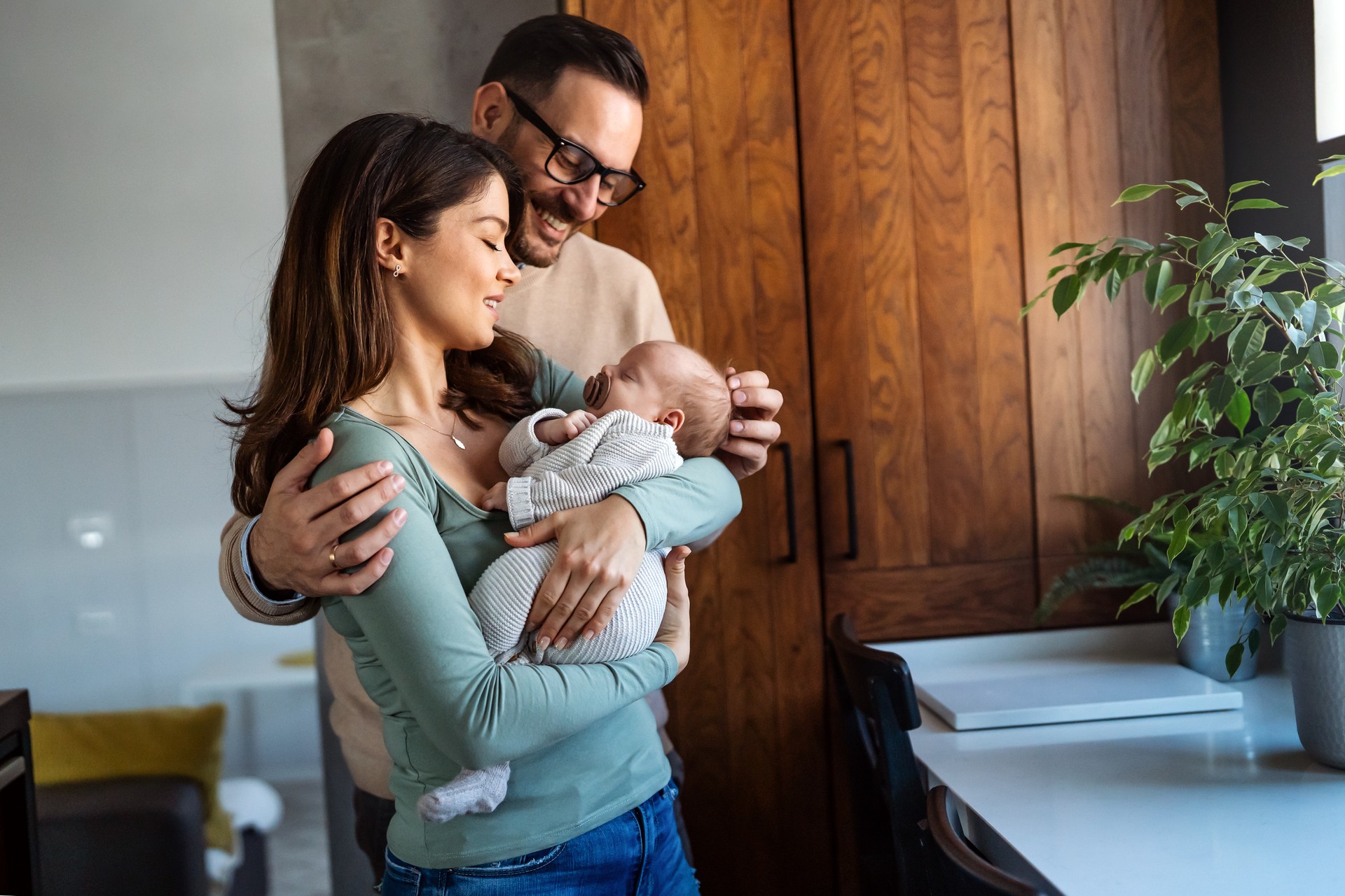 Portrait of young happy man and woman holding newborn cute babe dressed in white unisex clothing.