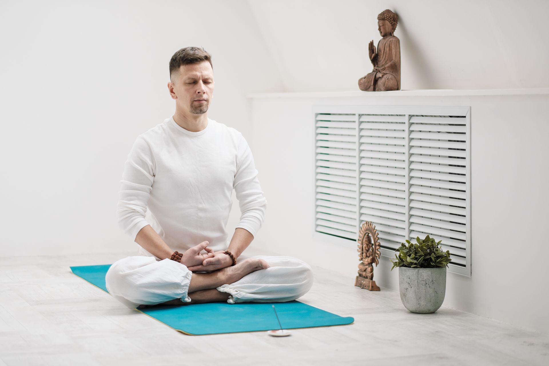 Male brunette with a beard in white clothes on a white background with his hands folded on his chest. Meditation and prayer, yoga on the yellow-blue rubber mat.